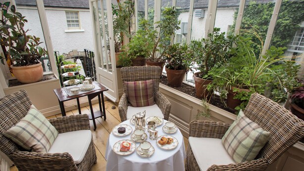 A conservatory with wicker furniture, a table set for tea, and potted plants. - Raheen House Hotel (Clonmel)