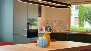 A modern kitchen with a wooden table and red chairs, a yellow vase, and a window with a view of greenery. - Family-friendly vacation apartment - four-legged friends also welcome! (Binzen)