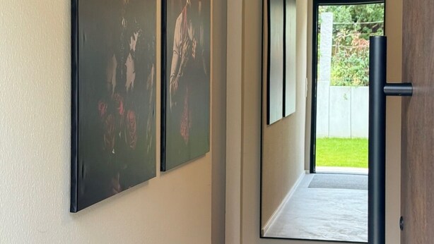 A hallway with three large paintings on the wall, a wooden door frame, and a view of a garden through an open door. - Family-friendly vacation apartment - four-legged friends also welcome! (Binzen)