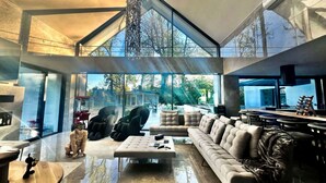 A spacious living area with a high ceiling, large windows, and a modern chandelier.