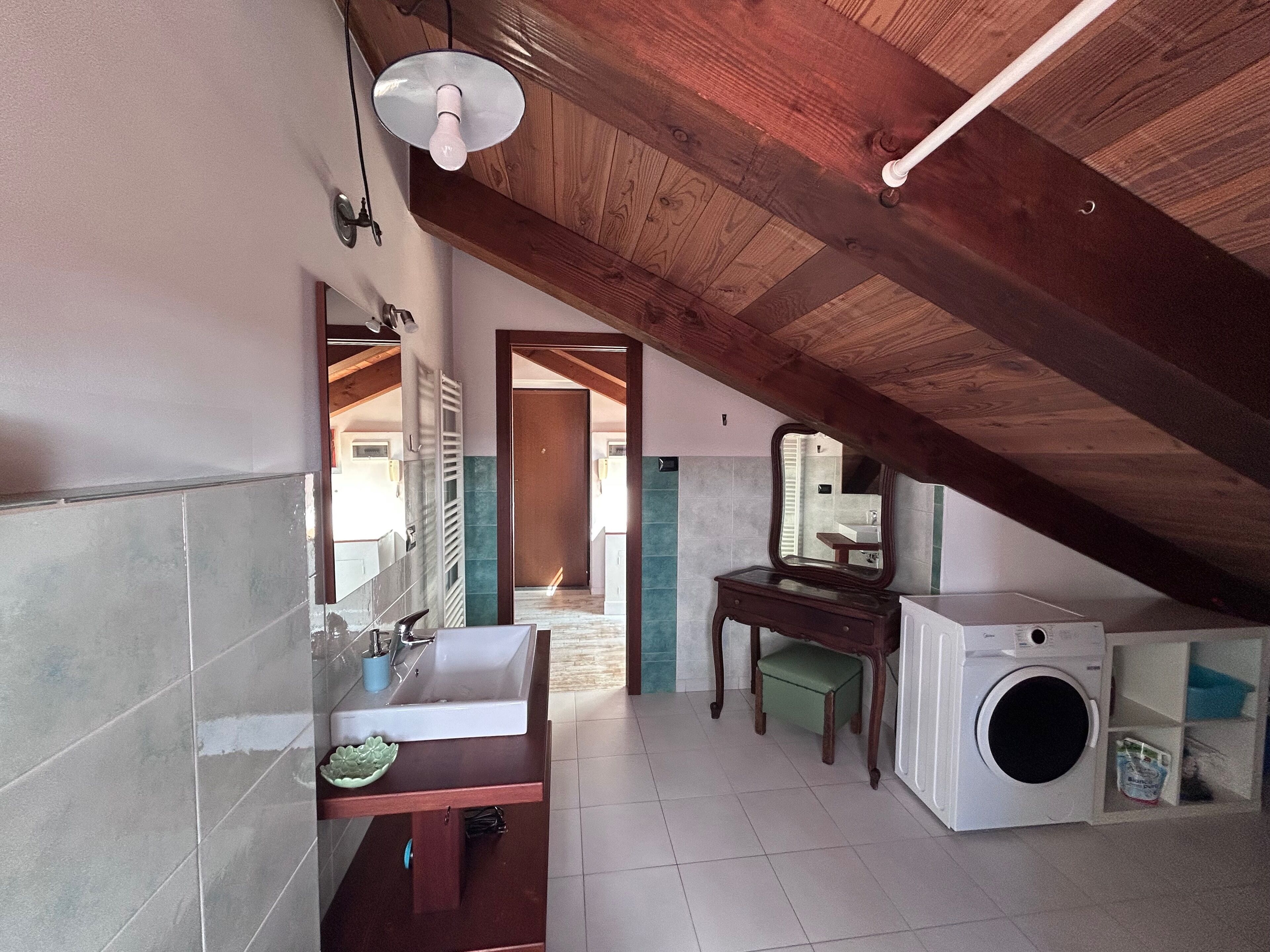 Un baño pequeño y rústico con techo de madera, un lavabo, un espejo y una lavadora.