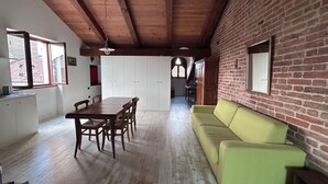 A dining area with a wooden table and chairs, a green sofa, and a brick wall.