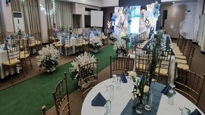 Un salón de banquetes con mesas redondas, centros de mesa florales y un escenario con fondo decorativo.