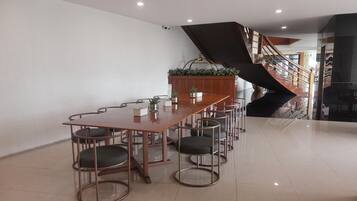 Un salón de conferencias con una larga mesa y seis sillas, una escalera y una planta en maceta.