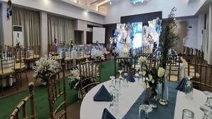 A banquet hall with round tables set for events, featuring white floral centerpieces and blue napkins.