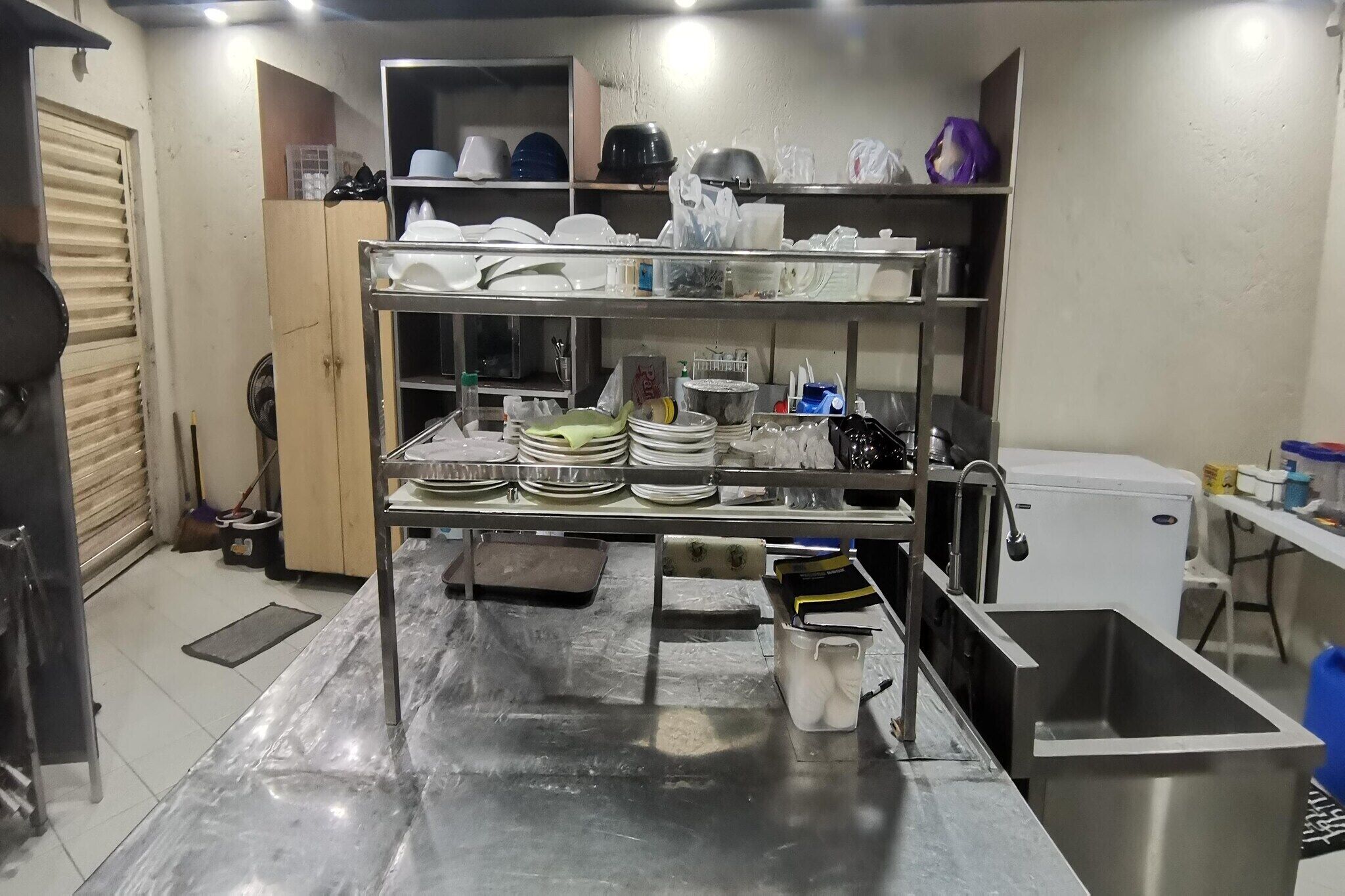A stainless steel kitchen with multiple shelves holding dishes and utensils.