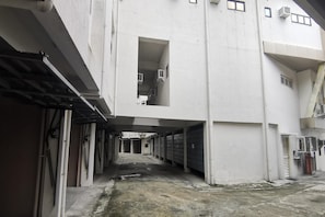 Un couloir bordé de portes de garage fermées, une porte centrale ouverte donnant sur un escalier et un sol en béton.