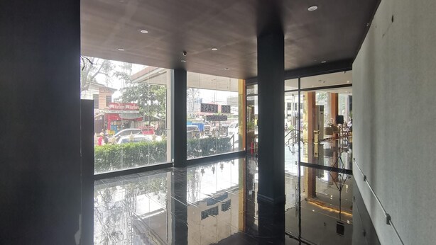 Un interior moderno con amplios ventanales, piso pulido y un espacio exterior visible con vehículos y edificios.