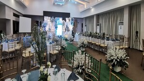 Un salón de banquetes con mesas redondas, sillas y centros de mesa florales.