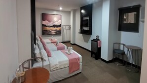 Habitación de hotel con dos camas, un cuadro, un televisor, una mesita y una silla.