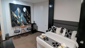 A hotel room with a bed, a desk with two chairs, a painting of mountains, and a night sky.