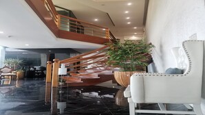 A modern interior with a polished black marble floor, a wooden staircase, and a white upholstered chair.