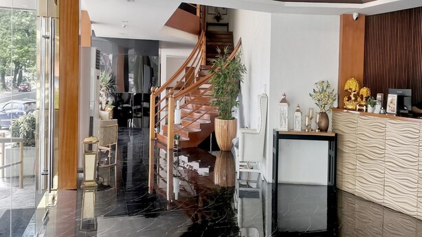 A modern hotel lobby with a wooden staircase, a reception desk, and a large potted plant.