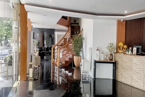 A modern hotel lobby with a wooden staircase, a reception desk, and a large potted plant. - Stylish Double in Pampanga, Clark Area (Pampanga)