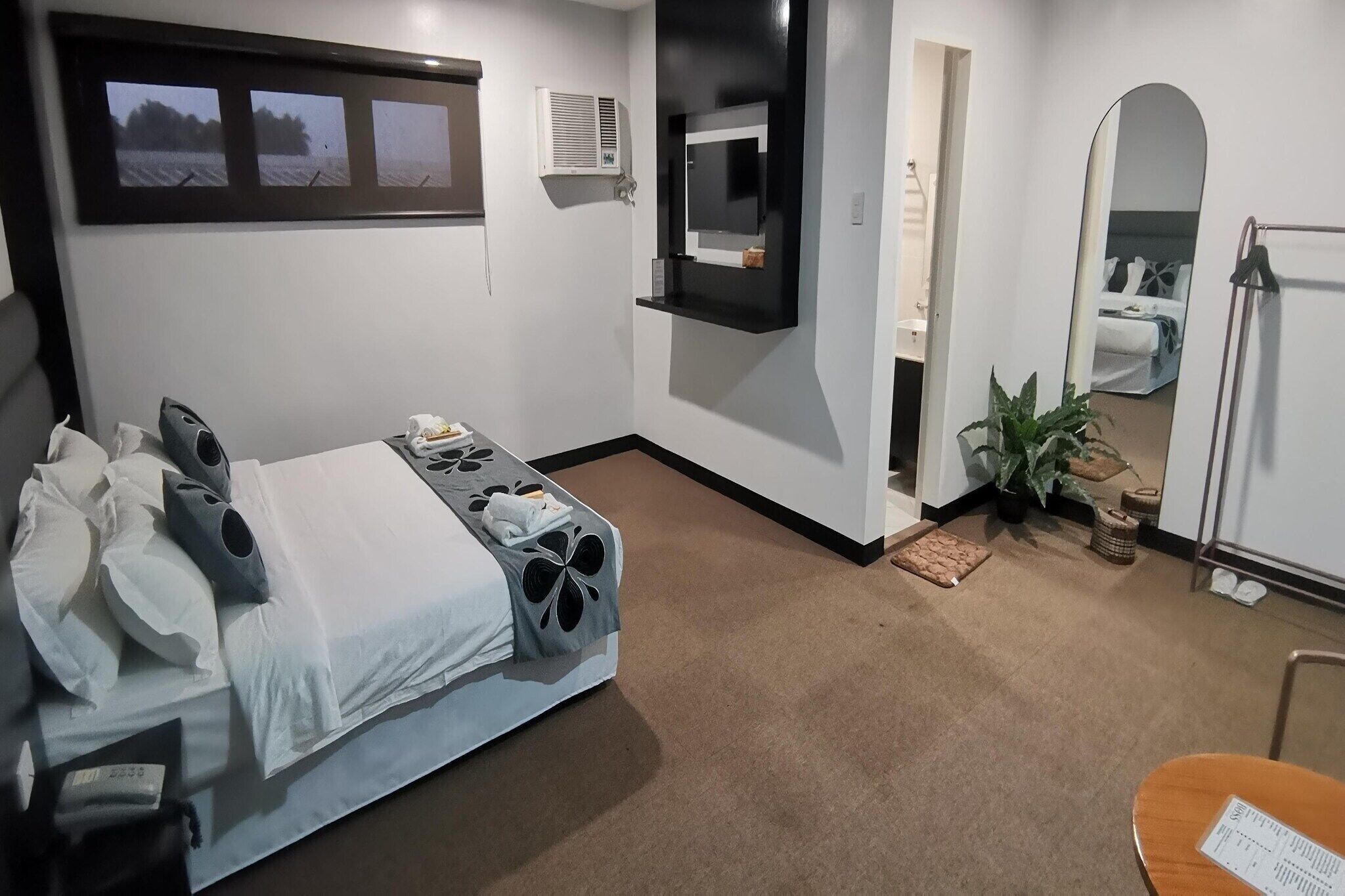 Una habitación de hotel con una cama, un televisor montado en la pared, un espejo y una planta en maceta.