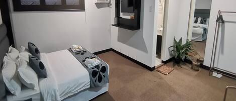 Una habitación de hotel con una cama, un televisor montado en la pared, un espejo y una planta en maceta.