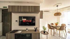 A modern living room with a flat-screen TV, a dining area with a table and chairs, and a small potted plant on the coffee table. - Seaside Serenity at 2BR home in San Pawl il-Baħar (San Pawl il-Baħar)
