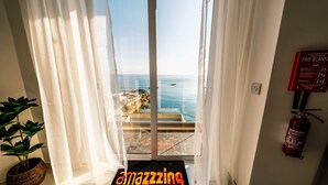 A room with a view of the sea through sheer curtains, a fire extinguisher on the wall, and a doormat with the word "amazing". - Seaside Serenity at 2BR home in San Pawl il-Baħar (San Pawl il-Baħar)