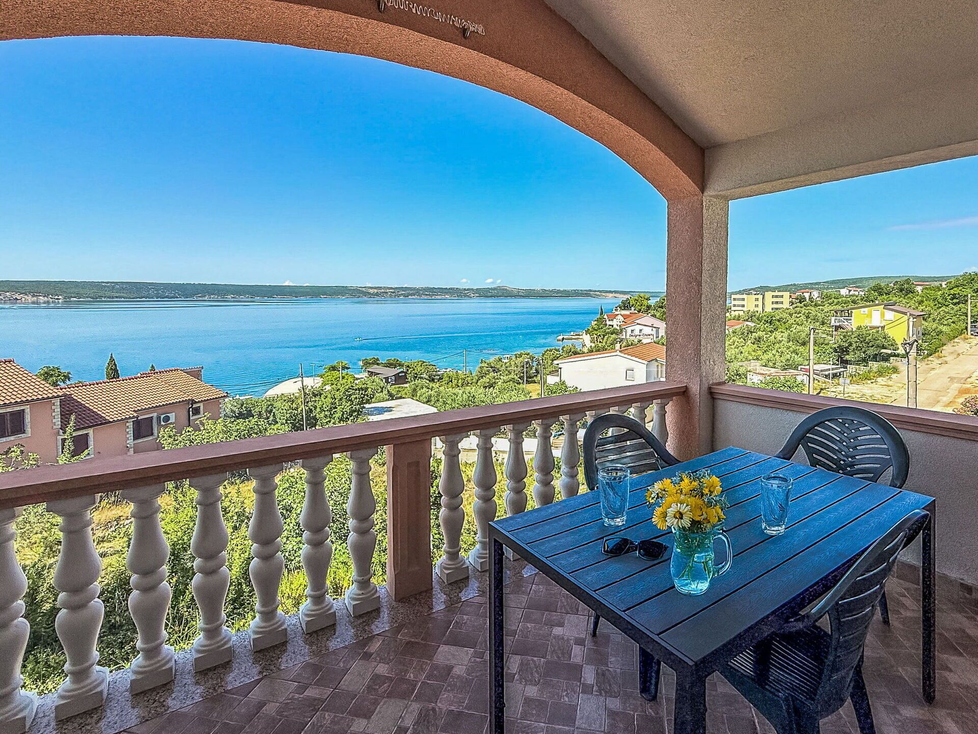 A balcony with a table, chairs, and a view of the sea.