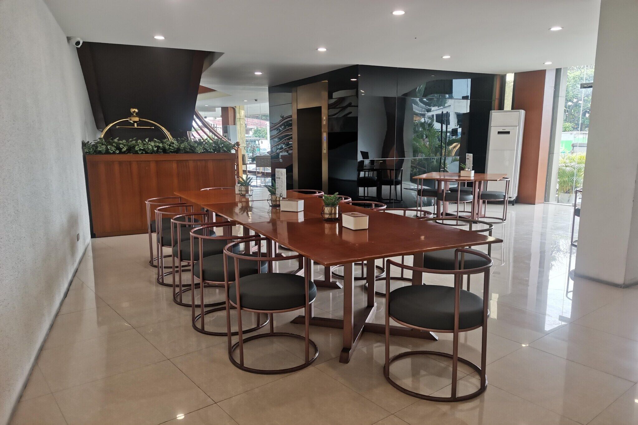 Een moderne hotel lobby met een houten receptiebalie, een grote glazen wand en een trap naar de verdiepingen erboven.