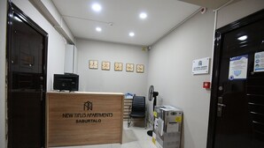 A reception area with a wooden desk labeled "NEW TIFLIS APARTMENTS SABUARTALO," a black office chair, a desk fan, and a fire alarm. - Apartment Tbilisi (Tbilisi)