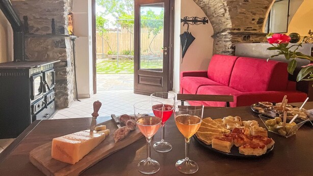 Una stanza accogliente con un arco in pietra che conduce a un giardino, un divano rosso e un tavolo con snack e bevande.