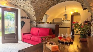 Un ambiente accogliente con soffitto in pietra, un divano rosso, un tavolo in legno con tagliere di formaggi, bicchieri da vino e una pianta in vaso.