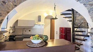 Una cucina con un arco in pietra, una ciotola di frutta sul bancone e un elettrodomestico rosso sullo sfondo.