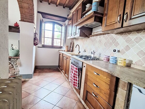 Een keuken met houten kastjes, een betegelde achterwand, een raam en een fornuis.