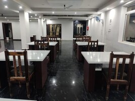 A spacious dining area with multiple tables and chairs, a polished black floor, and a ceiling fan.