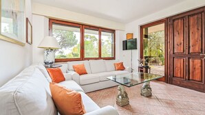 Ein Wohnzimmer mit einem weißen Sofa, orangefarbenen Kissen, einem Glastisch, einem Fernseher und einer Holztür.
