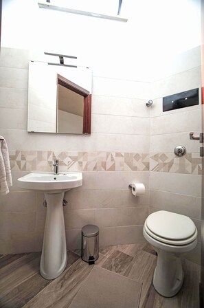 Un baño con lavamanos pedestal, inodoro y espejo con marco de madera.