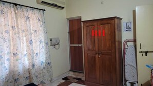 A room with a wooden wardrobe, a curtain with a floral pattern, and a wall-mounted air conditioner. - 1BHK apartment in a Holiday Resort close to the Beach with a common pool (Calangute)