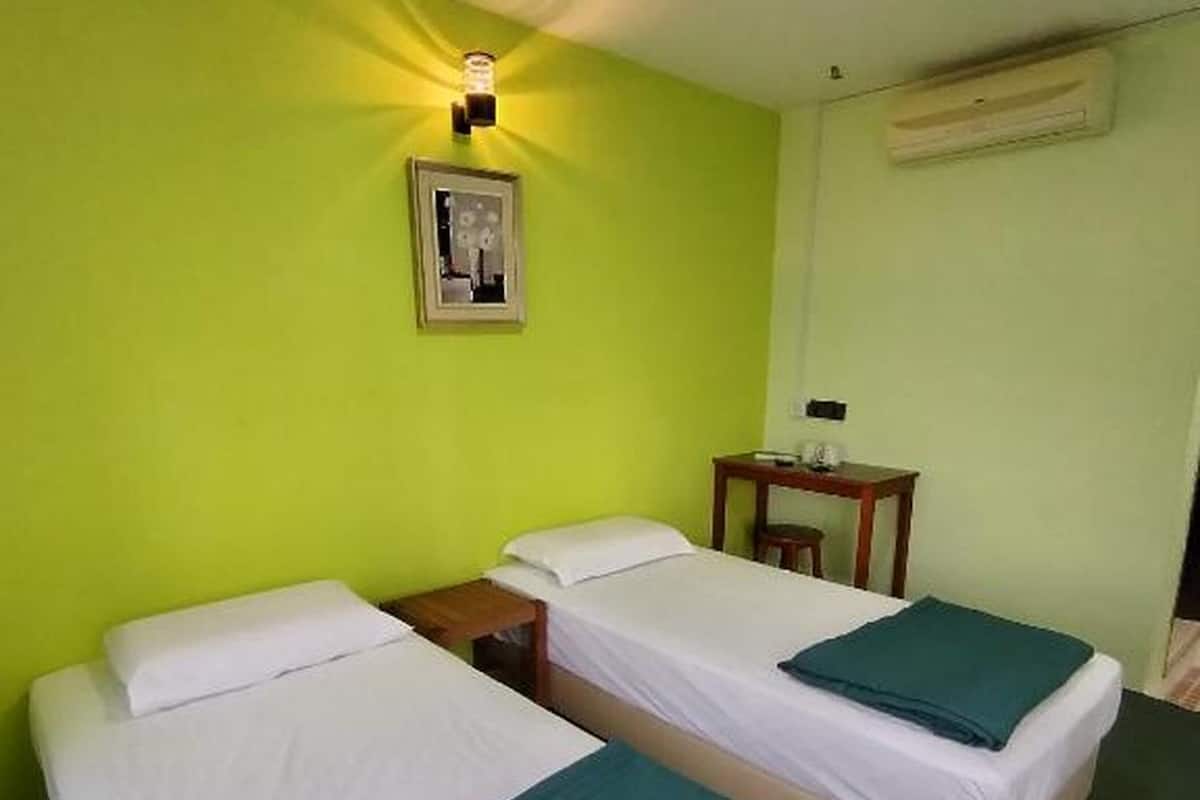 A room with two single beds, a small table, a wall-mounted air conditioner, and a picture on the wall.