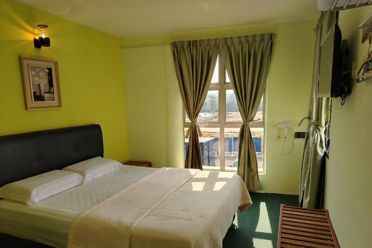 Une chambre d’hôtel avec un lit, une table de chevet, une fenêtre avec des rideaux et un téléphone fixé au mur.