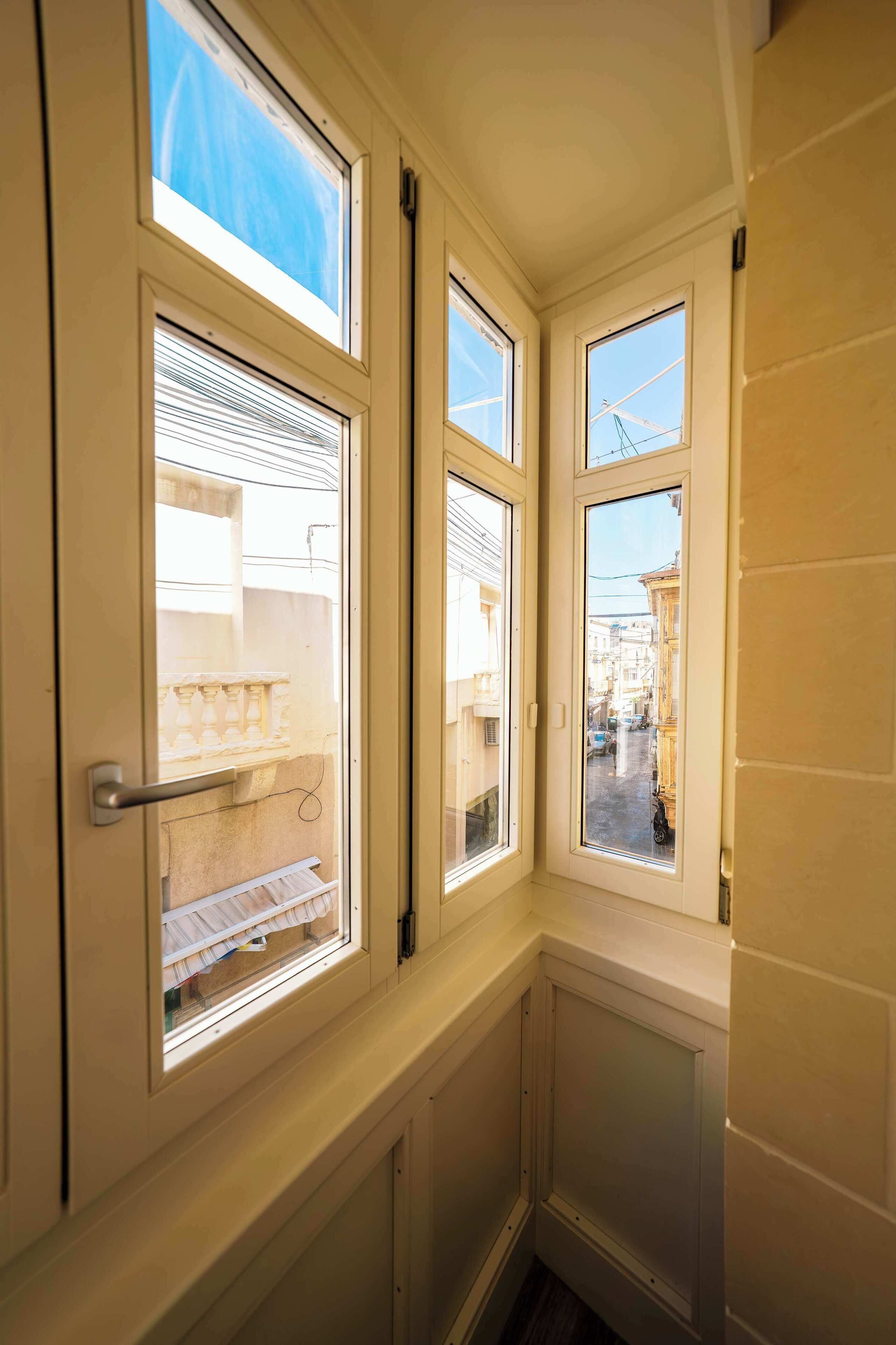 A corner room with three windows, a radiator, and a view of buildings outside.