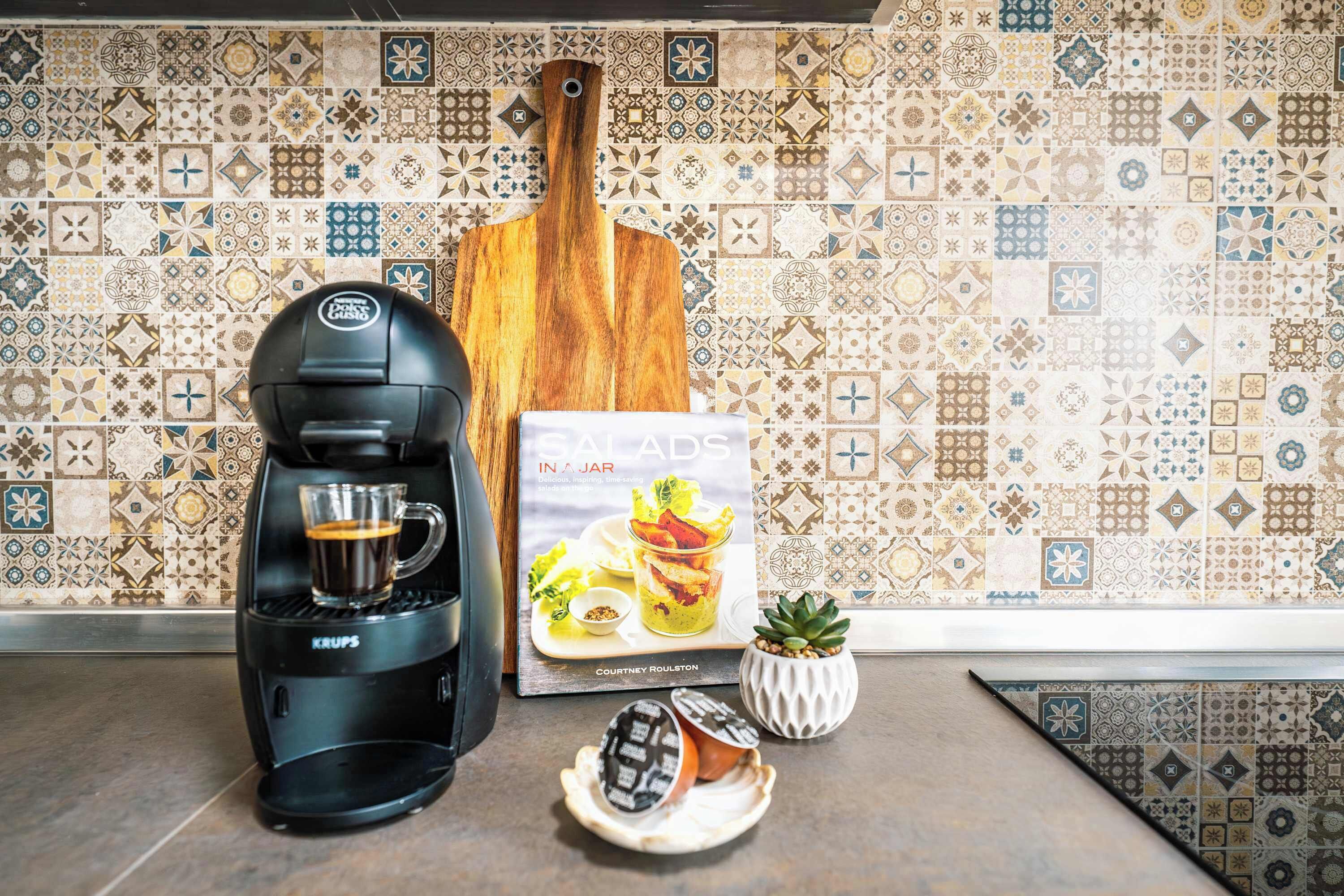 Een koffiezetapparaat, een kookboek en een kleine potplant op een keukentafel.
