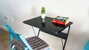 Une chaise de couleur bleu-vert avec un siège et un dossier rembourrés, une petite plante en pot et une pile de livres sur une table noire.
