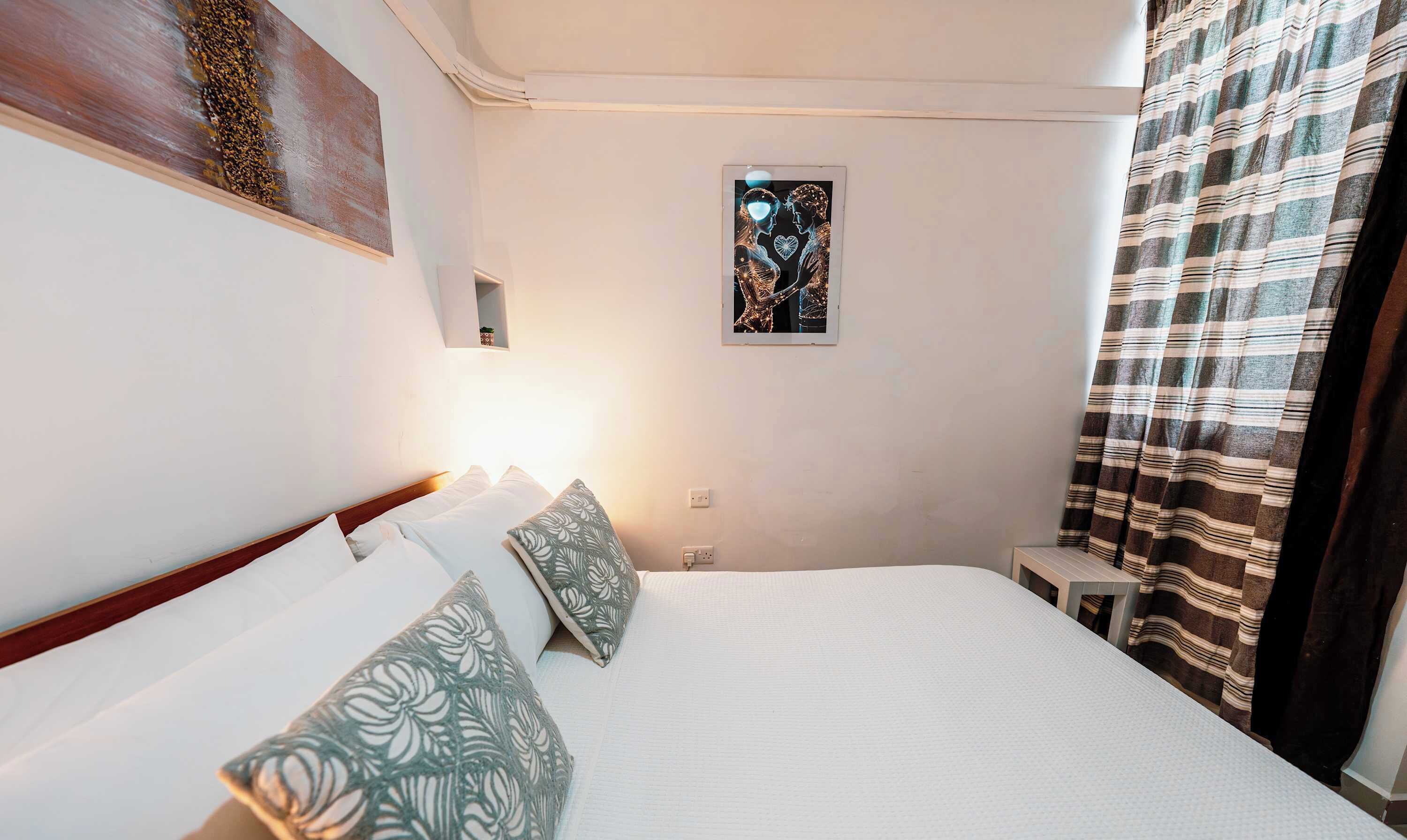 A hotel room with a bed, pillows, a wall art piece, and a curtain.