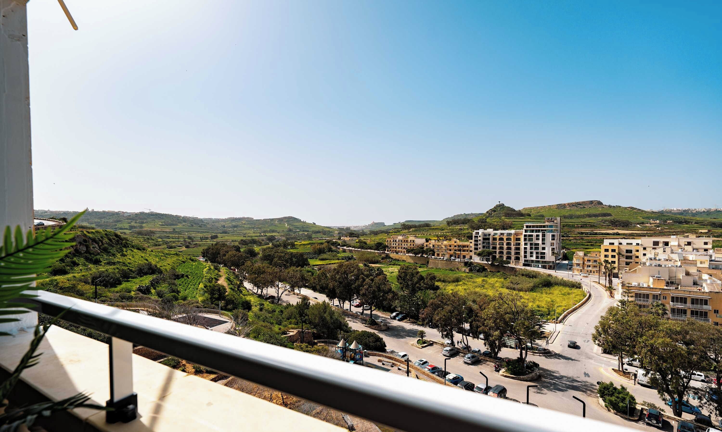 A balcony with a view of a cityscape, including buildings and a green landscape.