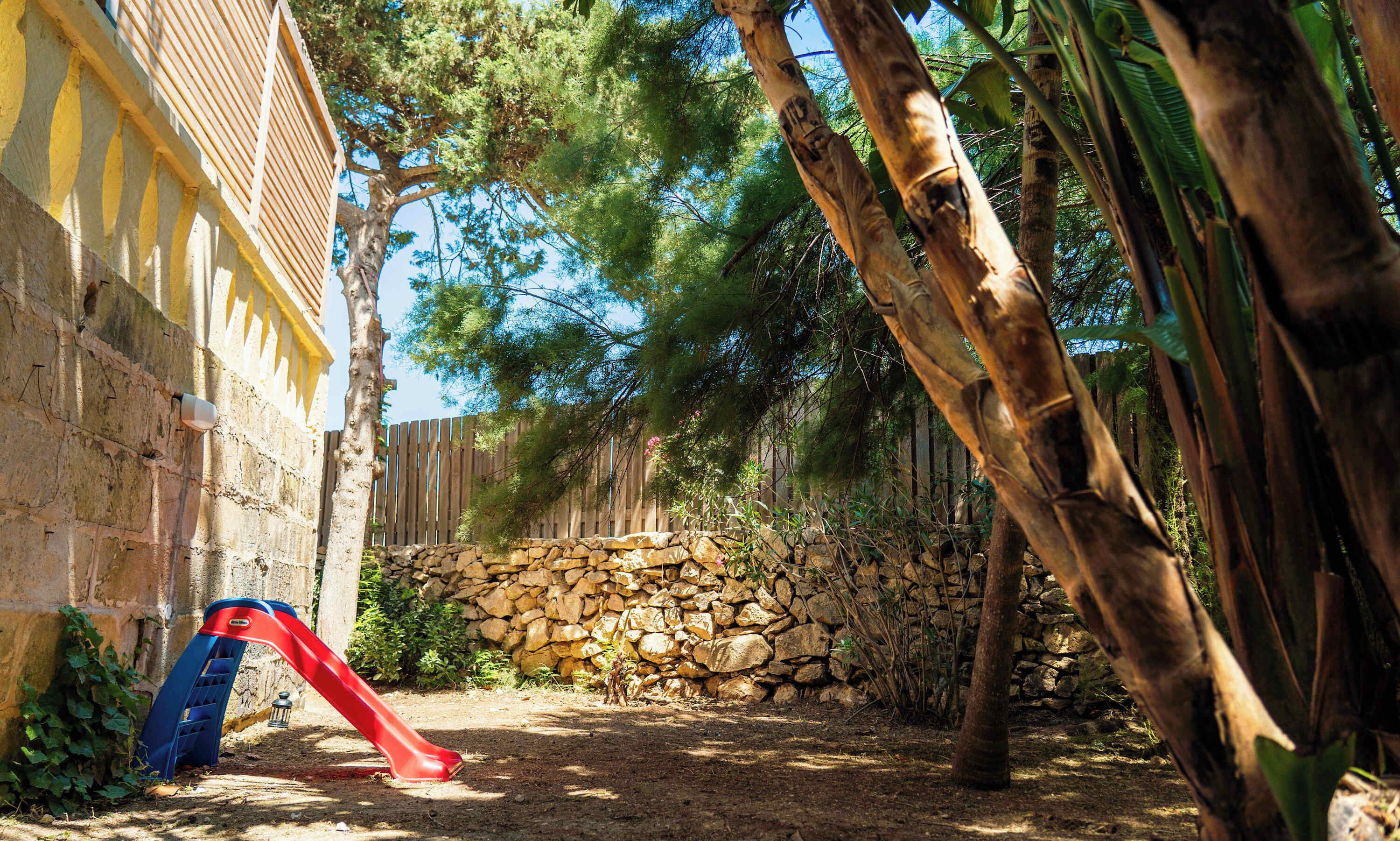 Un mur de pierres, un toboggan rouge et une clôture en bois dans un espace aménagé en jardin.