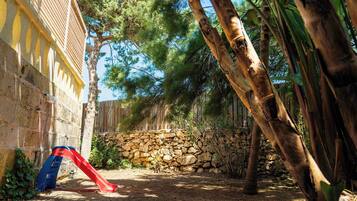 Un mur de pierres, un toboggan rouge et une clôture en bois dans un espace aménagé en jardin.