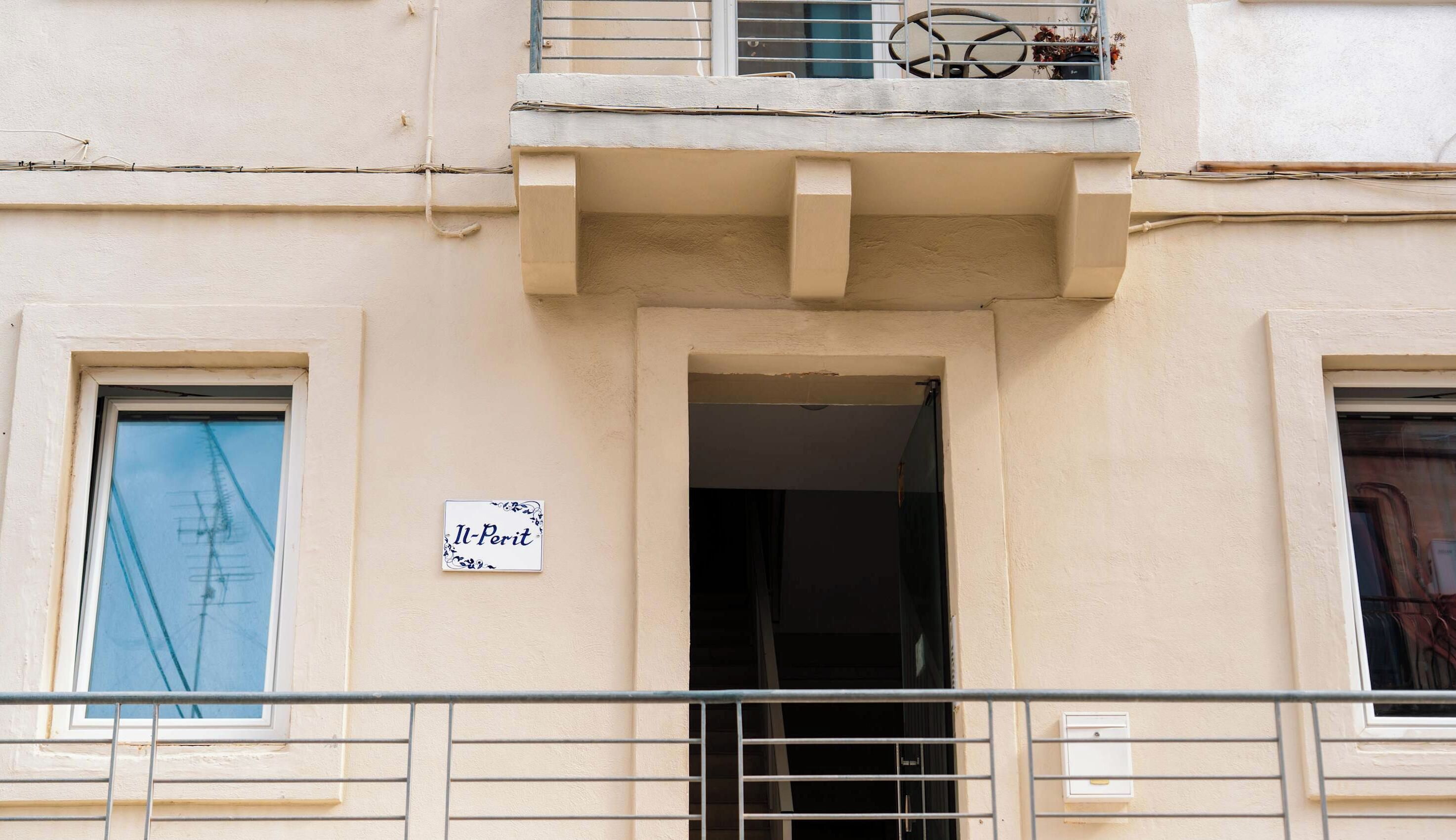 A building facade with a balcony, a door, and a sign reading 'Il-Perit'.