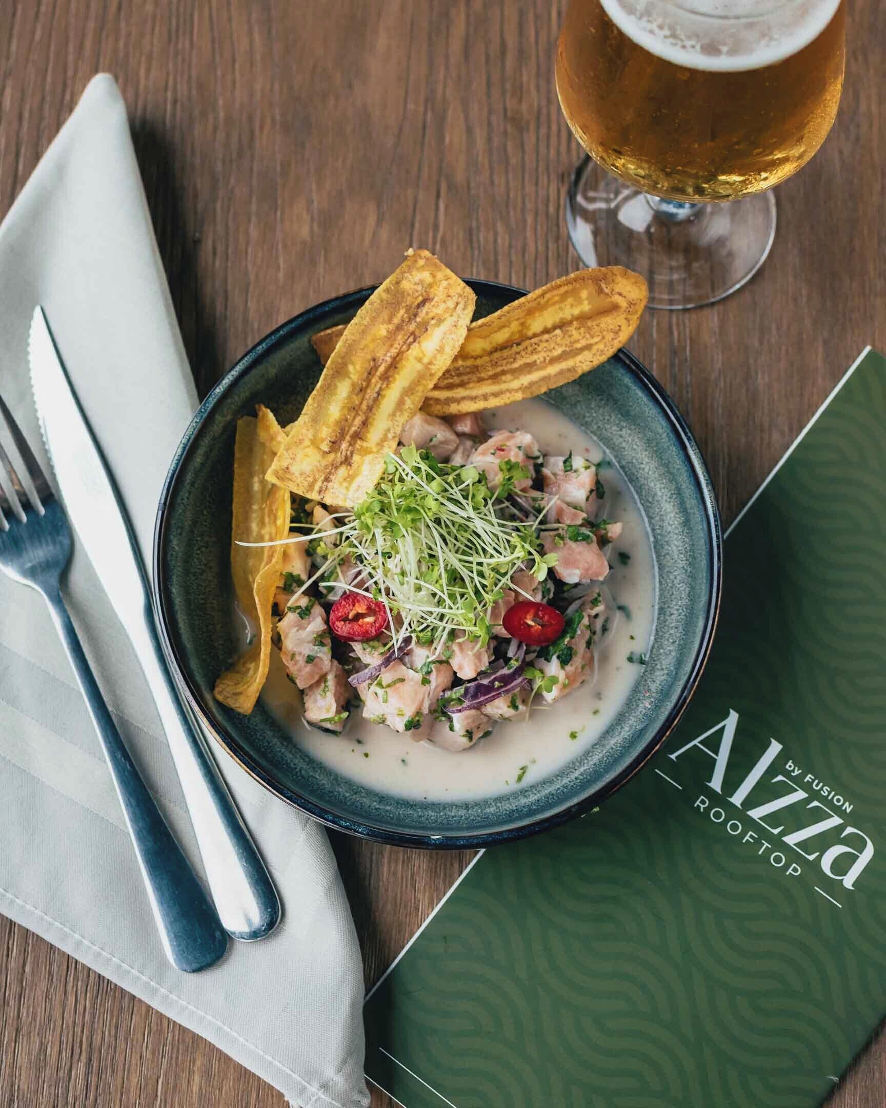 A bowl of food with a glass of beer, a napkin, and a menu on a wooden table.