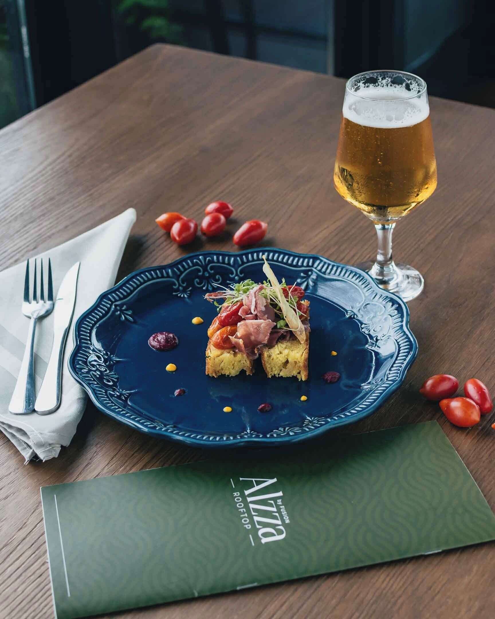 A table with a blue plate of food, a glass of beer, and a green menu.