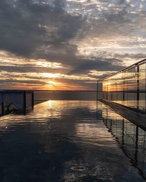 A waterfront deck with a glass railing overlooking the sea, a sunset in the background, and a clear sky. - Alula Hotel Encarnacion (Encarnación)