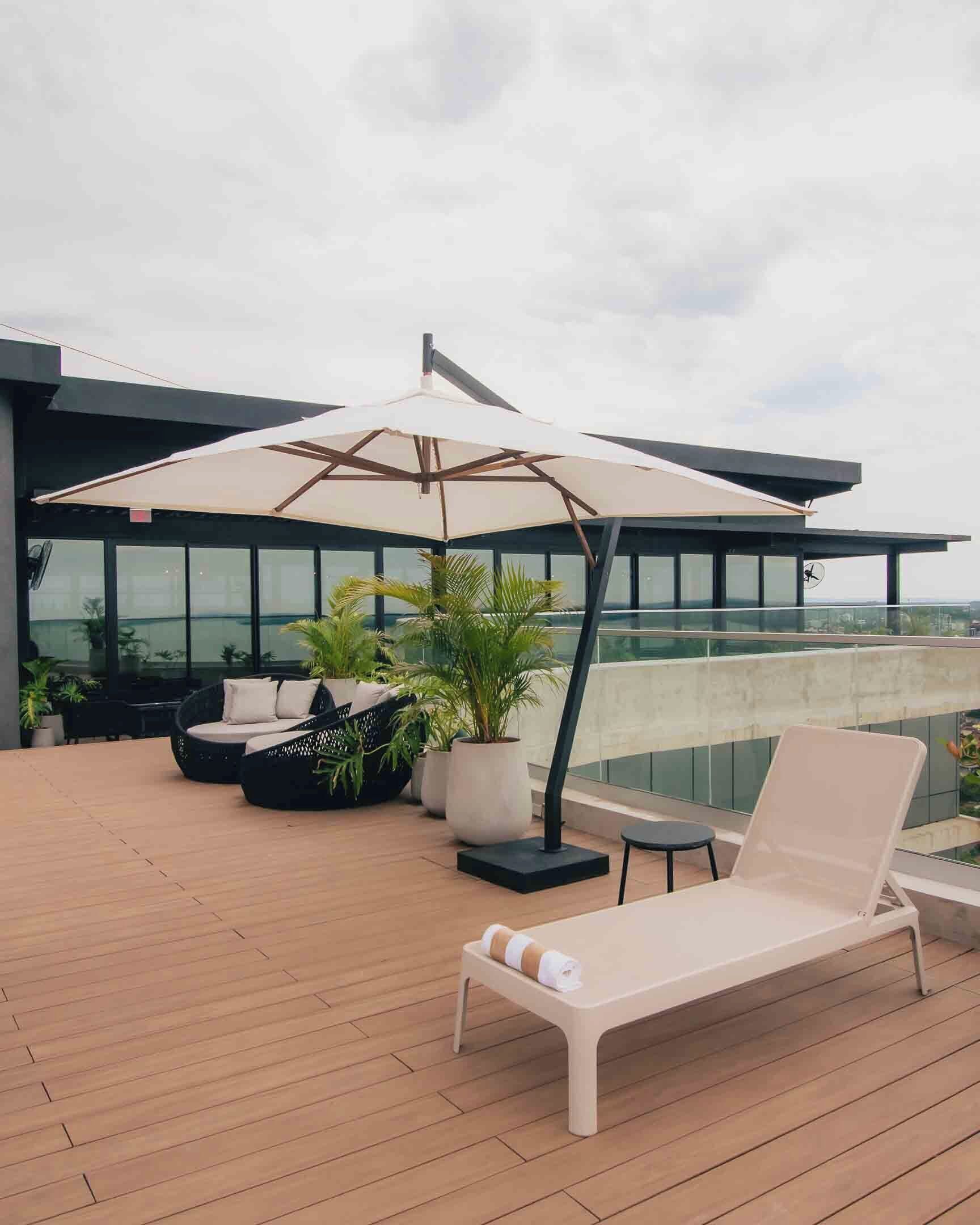 A rooftop terrace with a lounge chair, a cushioned seating area, and a large umbrella.