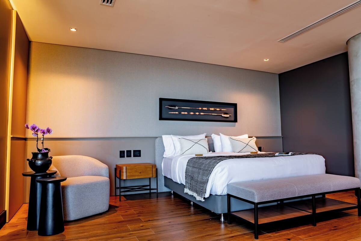 A modern bedroom with a bed, bedside tables, a bench, and a wall-mounted artwork.