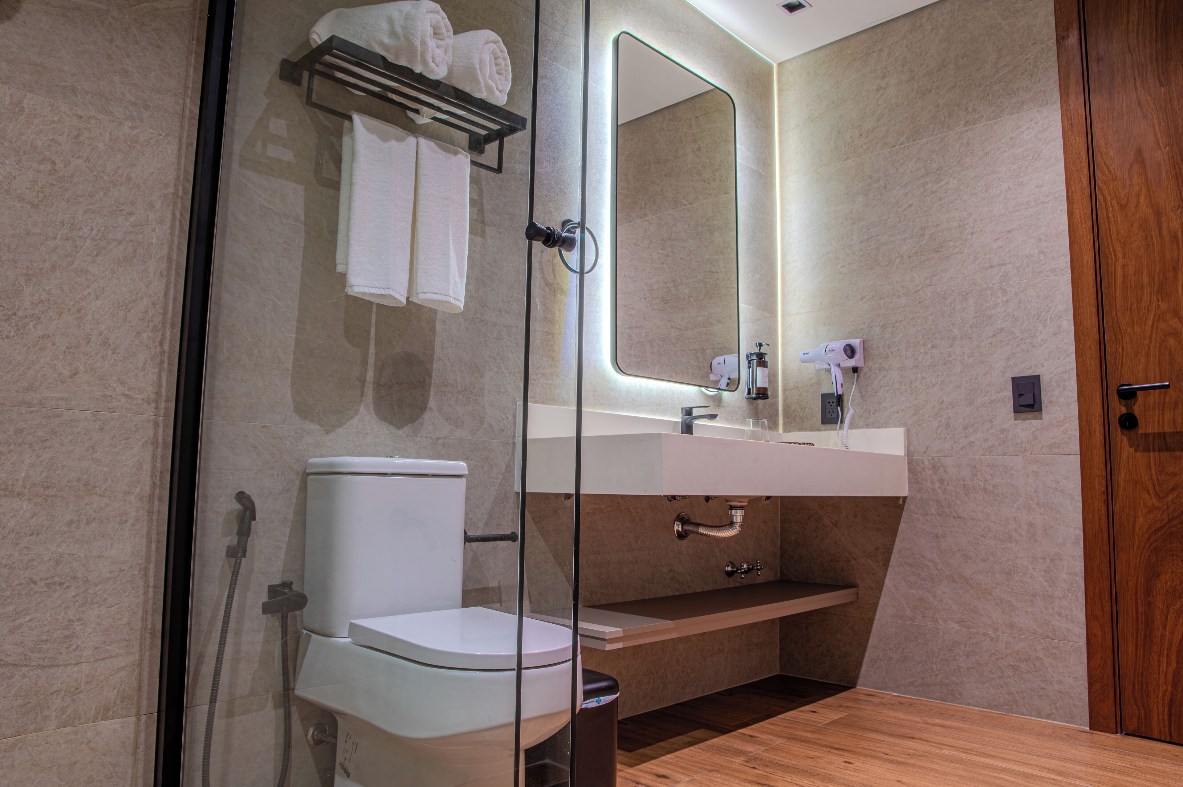 A modern bathroom with a glass-enclosed shower, a white toilet, a sink with a mirror, and a wooden vanity.