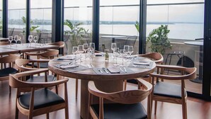 A restaurant with round tables, chairs, and a view of the water. - Alula Hotel Encarnacion (Encarnación)